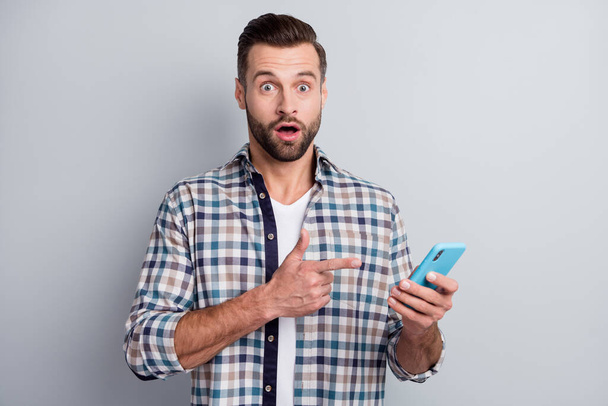 Photo portrait of amazed guy pointing finger smartphone opened mouth isolated on grey color background - 写真・画像