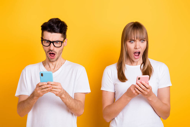 Photo of pretty impressed young couple wear white t-shirt spectacles reading modern gadgets isolated yellow color background - Foto, afbeelding