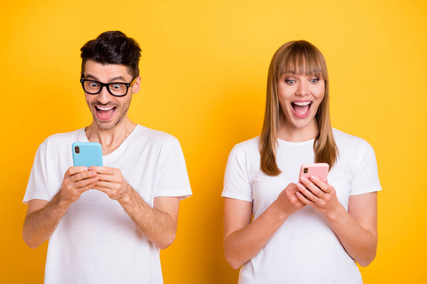 Photo of charming shocked two persons dressed white t-shirt glasses writing modern devices isolated yellow color background - Foto, Bild