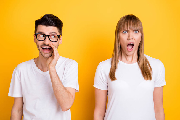 Photo of shocked funny young couple wear white t-shirt spectacles arm lips telling secret isolated yellow color background - Foto, afbeelding