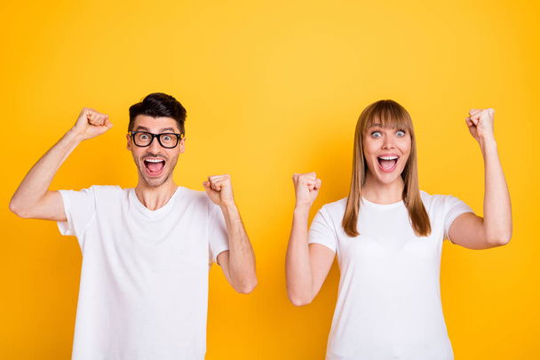 Photo of sweet lucky young couple wear white t-shirt spectacles rising fists isolated yellow color background - Фото, зображення