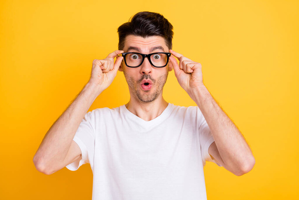 Photo of impressed funny young man wear white t-shirt arms spectacles big eyes isolated yellow color background - Foto, immagini