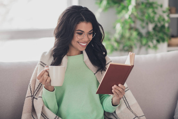 Portrét atraktivní veselé tmavé pleti dáma držet hrnek na kávu kniha zářící úsměv přikrývka na ramenou uvnitř - Fotografie, Obrázek