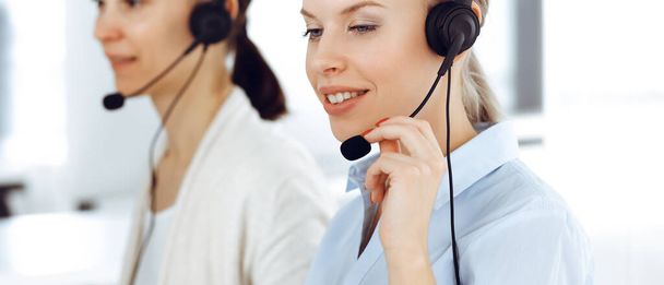 Blond woman call operator is using computer and headset for consulting clients online. Group of diverse people working as customer service occupation. Business concept - 写真・画像
