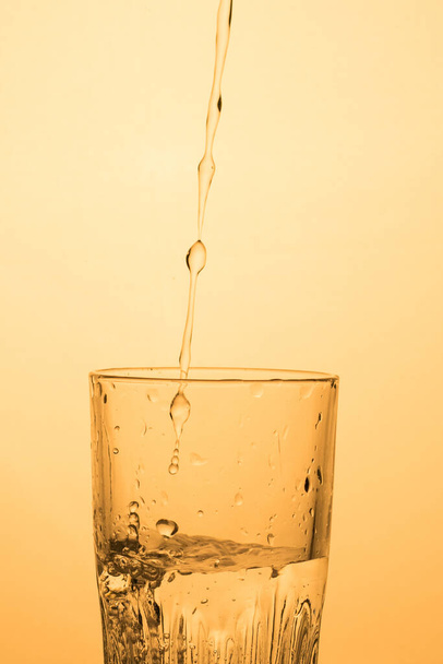 Ein Wasser- oder Wodkastrom ergießt sich in ein Glas mit Spritzern, warmem Schatten, vertikalem Format mit Kopierraum. - Foto, Bild