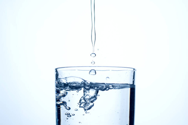 Wasserstrahl oder Alkohol ergießt sich in ein Glas mit Spritzern und Blasen, Kopierraum. - Foto, Bild