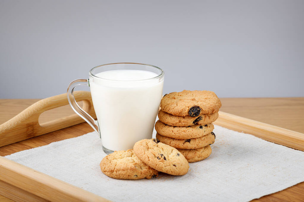 Ένα φλιτζάνι γάλα και μπισκότα με σταφίδες σε ξύλινο δίσκο - Φωτογραφία, εικόνα