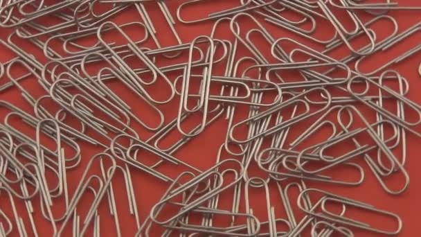 Silver paper clips rotating on a red background. - Footage, Video