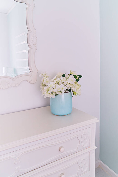 Spiegel in gesneden houten frame en vaas met bloemen in lichte kamer, vintage interieur. - Foto, afbeelding