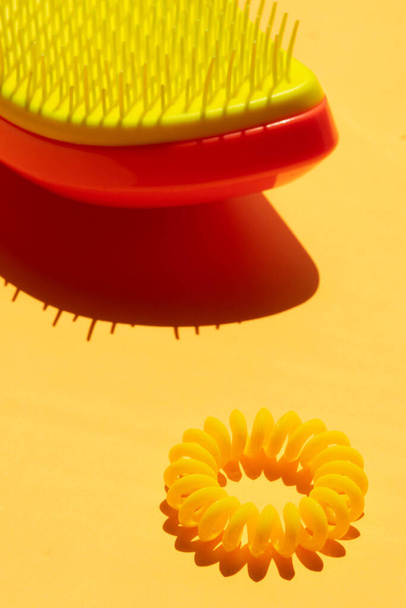 Gelber orangefarbener Kunststoff-Haarkamm und gelbe Kunststoff-Haarbinde auf sonnigem gelbem Tisch. - Foto, Bild