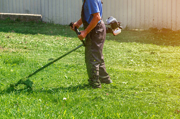 Ouvrier en pantalon de protection tonds l'herbe verte sur la pelouse avec tondeuse autonome - Photo, image