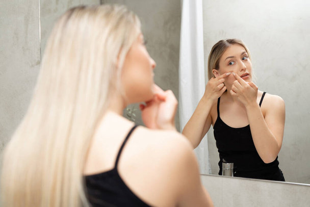 beautiful young woman in the bathroom by the mirror squeezes out pimples - Foto, afbeelding