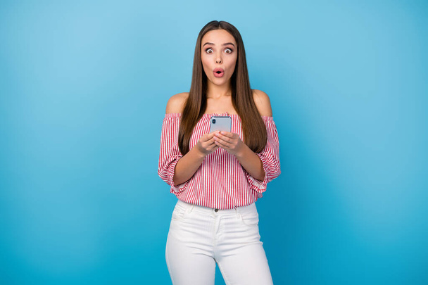 Portrait of attractive amazed straight-haired girl using cell reading news isolated over bright blue color background - Photo, image