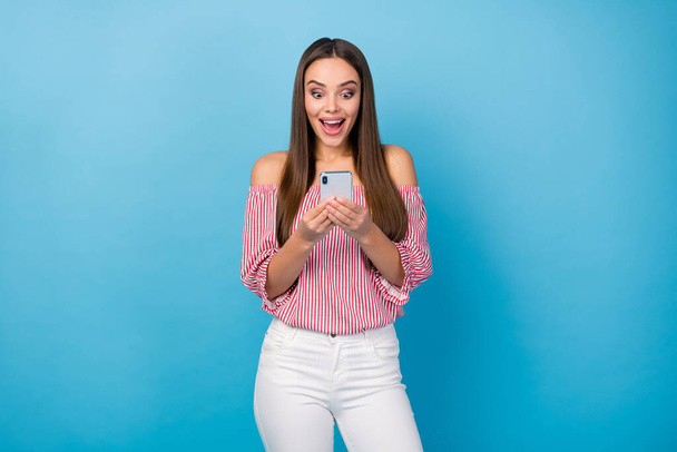 Portrait of astonished blogger girl use cellphone omg wear white red pants isolated over blue color background - Foto, imagen