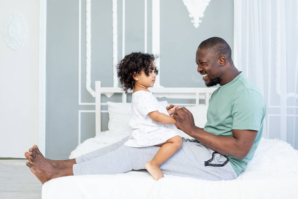 feliz afro-americano papá y hija sonriendo en la cama en casa, feliz familia - Foto, Imagen