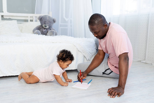 Il padre afroamericano insegna al figlio di suo figlio a disegnare con le matite sul pavimento a casa. - Foto, immagini
