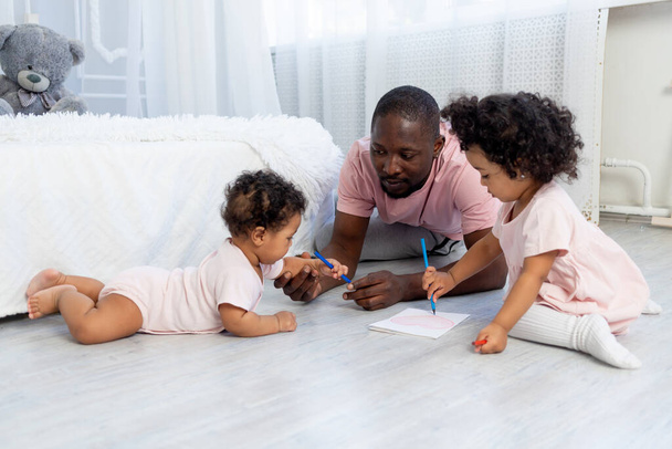 afro-amerykański tata uczy dzieci jak rysować ołówki na podłodze w domu - Zdjęcie, obraz