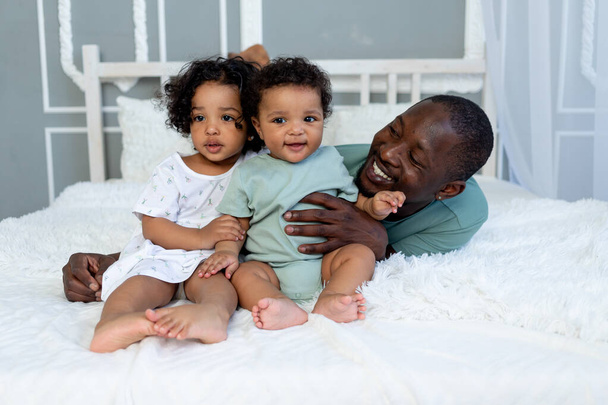 afrykańsko-amerykański tata bawi się z dziećmi w domu na łóżku w sypialni i przytula, miłość ojca - Zdjęcie, obraz