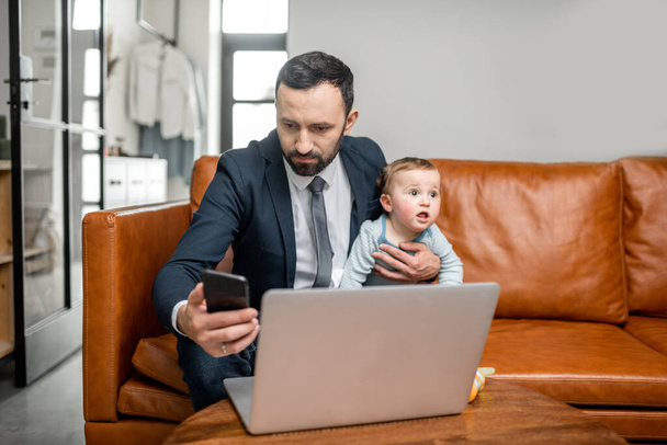 Jovem pai trabalhando em um laptop e falando por telefone - Foto, Imagem