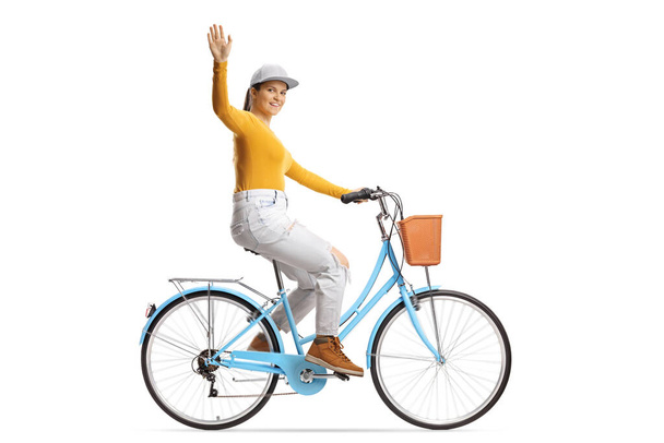 Full length profile shot of a young female riding a city bicycle and waving at camera isolated on white background - Foto, imagen