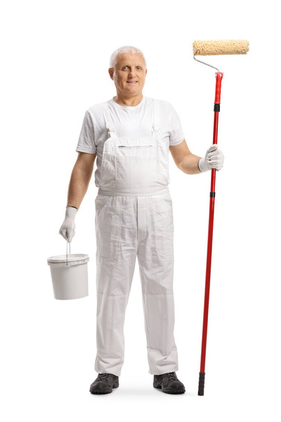 Full length portrait of a mature house painter holding a bucket and a paint roller isolated on white background - Foto, afbeelding