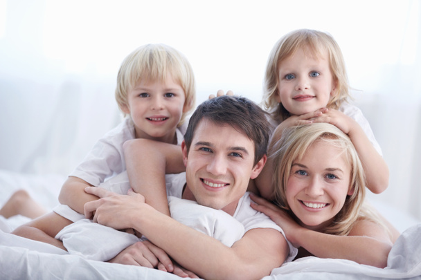 Perhe, jolla on kaksi lasta sängyssä makuuhuoneessa
 - Valokuva, kuva