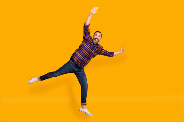 Full length photo of funny mature man raise hands leg good mood isolated on shine bright yellow color background - Fotografie, Obrázek