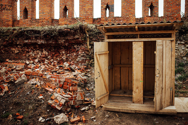 eine alte schmutzige Holztoilette inmitten der Ruinen. Eine Latrine in einem Armenviertel zwischen Müll und kaputten Ziegeln. veraltete Toilette - Foto, Bild