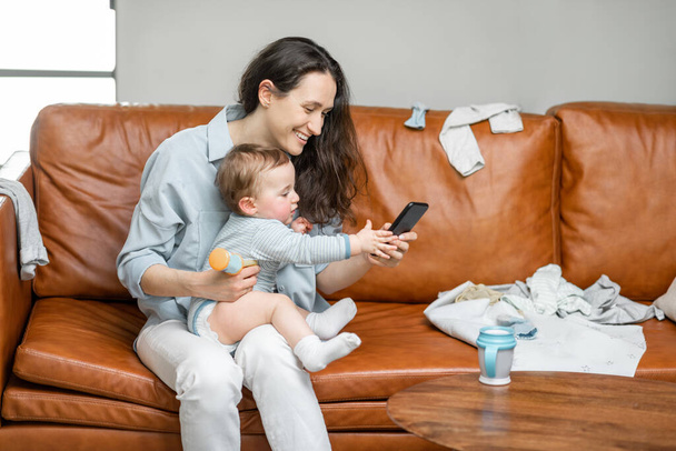 Young mom sitting with newborn son on sofa. - Photo, Image
