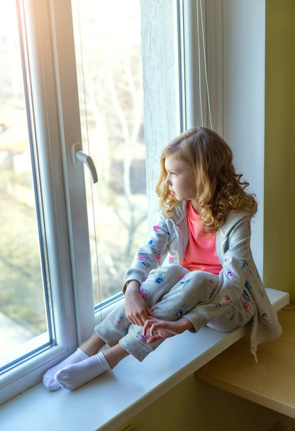 pretty girl sitting on the windowsill and looking out the window - Foto, imagen