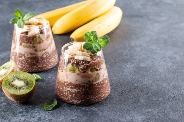 Cocoa chia seed pudding with kiwi and banana on dark gray table. Healthy vegan breakfast with copy space. - Photo, Image