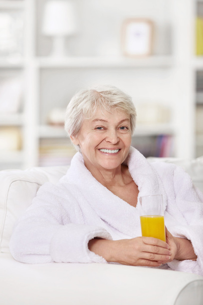 Smiling attractive woman in a bathrobe with a glass of juice - Foto, imagen