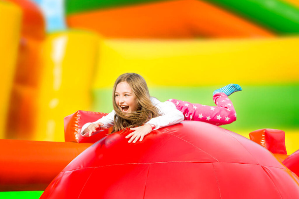 Щаслива маленька дівчинка розважається в надувному замку під час стрибків. Барвистий ігровий майданчик
. - Фото, зображення