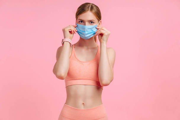Vonzó fitness nő védő maszk COVID vírus, mosolygós nő fitness edzés után, rózsaszín alapon, egészséges életmód koncepció - Fotó, kép