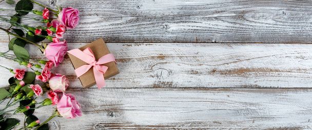 Echt rosa Rosen und Nelkenblüten mit Geschenkbox auf der linken Seite der rustikalen Holzplanken für Muttertag oder Valentinstag  - Foto, Bild