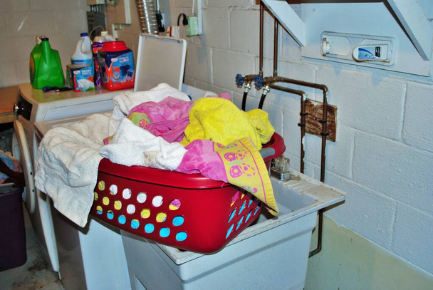 地下のランドリールームで洗浄する必要がある汚れたタオルでいっぱいのバスケット。 - 写真・画像