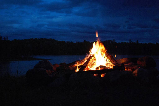 camp fire burning in a fire pit next to the lake - Photo, Image