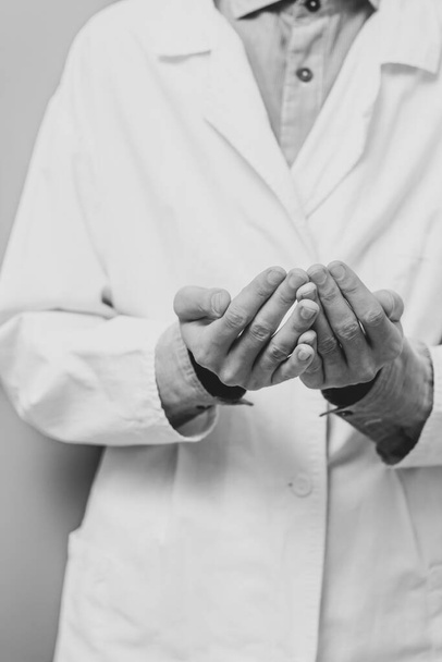 A young man in a white medical coat raised his hands and prayed. Medical gloves. The doctor is praying. A Muslim makes dua. Black and white photo - Fotoğraf, Görsel