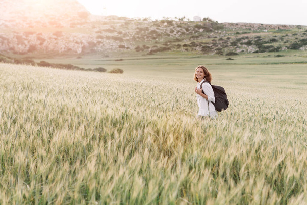 A young traveler with a backpack walks across a field of ears. - Foto, immagini
