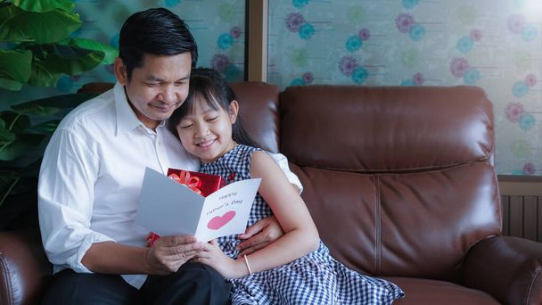 Vader knuffelt en leest de briefkaart die zijn dochter gelukkig in de kamer heeft gegeven.Concept van gelukkige vaderdag - Foto, afbeelding