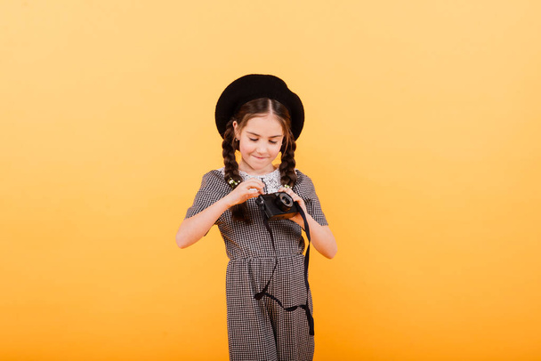 Portrait of a baby girl holding photo camera isolated on yellow background - Photo, Image
