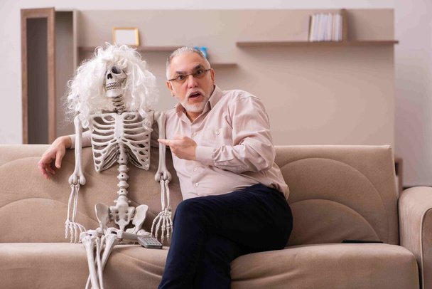 Ο γέρος κάθεται στον καναπέ με τον γυναικείο σκελετό. - Φωτογραφία, εικόνα