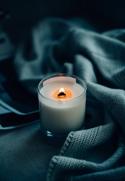 Burning candle in glass with wooden wick, handmade natural wax candle with knitted blanket - Foto, Imagen