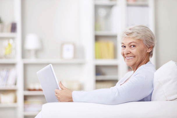 Mulher idosa sorridente no sofá com um laptop
 - Foto, Imagem