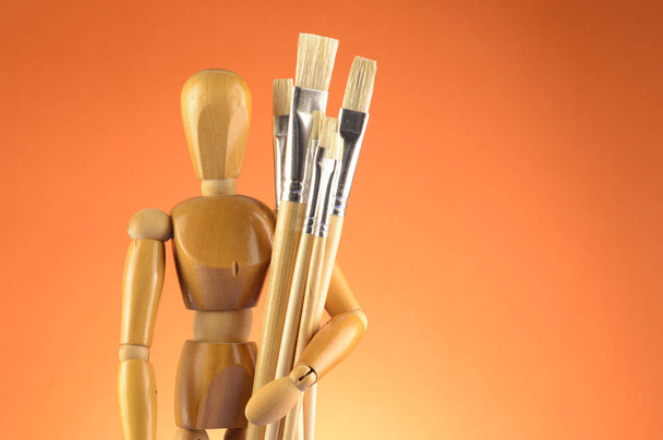 An Artists wooden Dummy Mannequin stands with some dry paintbrushes over an orange background. - Photo, Image
