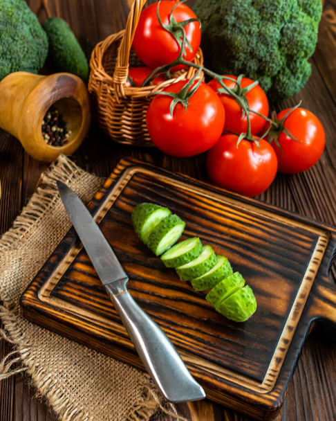 新鮮なキュウリはまな板の上でスライスにカットします。サラダの具材を用意する。テーブルの上の新鮮な野菜。有機農産物。ブロッコリー、トマト、市場からキュウリ。健康食品のコンセプト - 写真・画像