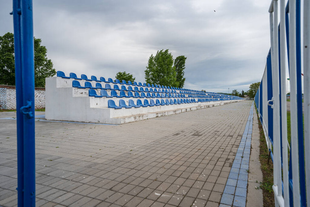 Üres tribün, kék székekkel, emberek nélkül a kis stadionban a felhős napokon. - Fotó, kép