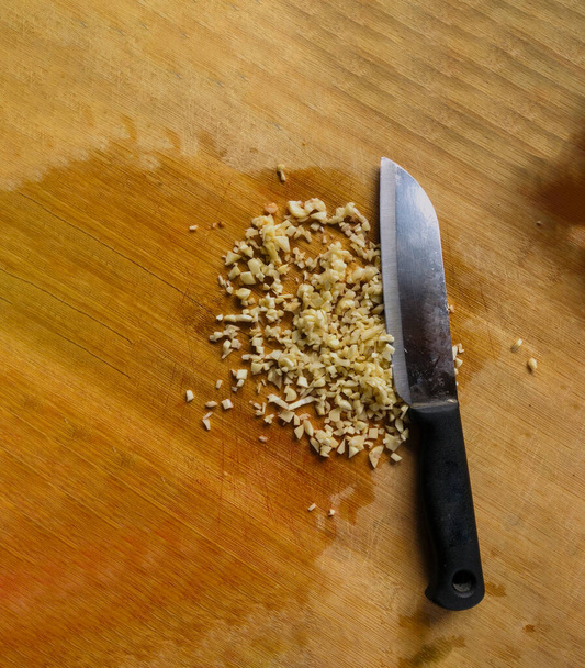 Мелко нарезанный чеснок на деревянной доске, нарезанные чесночные клещи - Фото, изображение