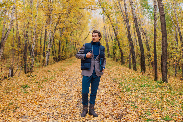 Tall handsome man dressed in a brown jacket walking in the autumn alley - Foto, immagini