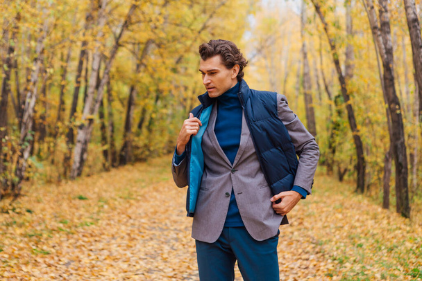 Tall handsome man dressed in a brown jacket walking in the autumn alley - Фото, зображення